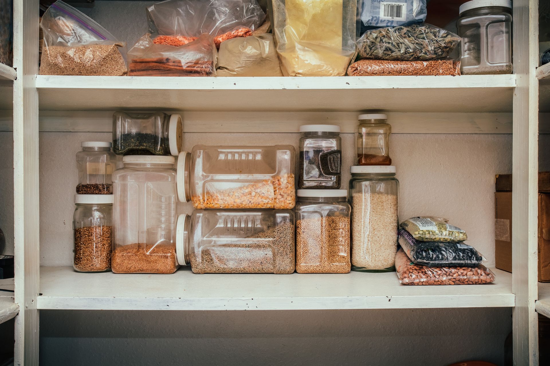 Pantry shelves filled with clear jars and bags of various dry goods, including grains and beans, neatly arranged.