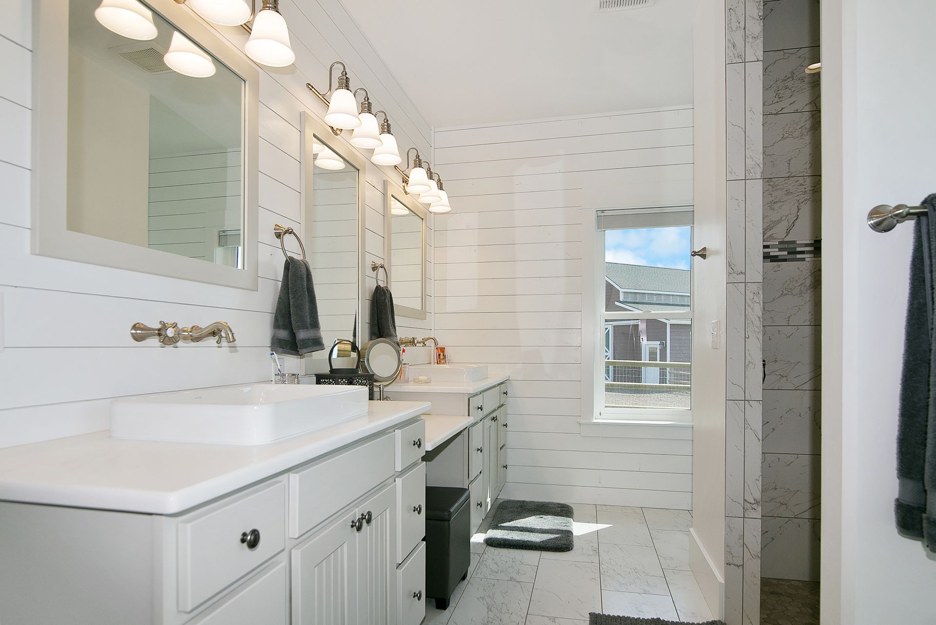 White bathroom with dual sinks, mirrors, and a window.