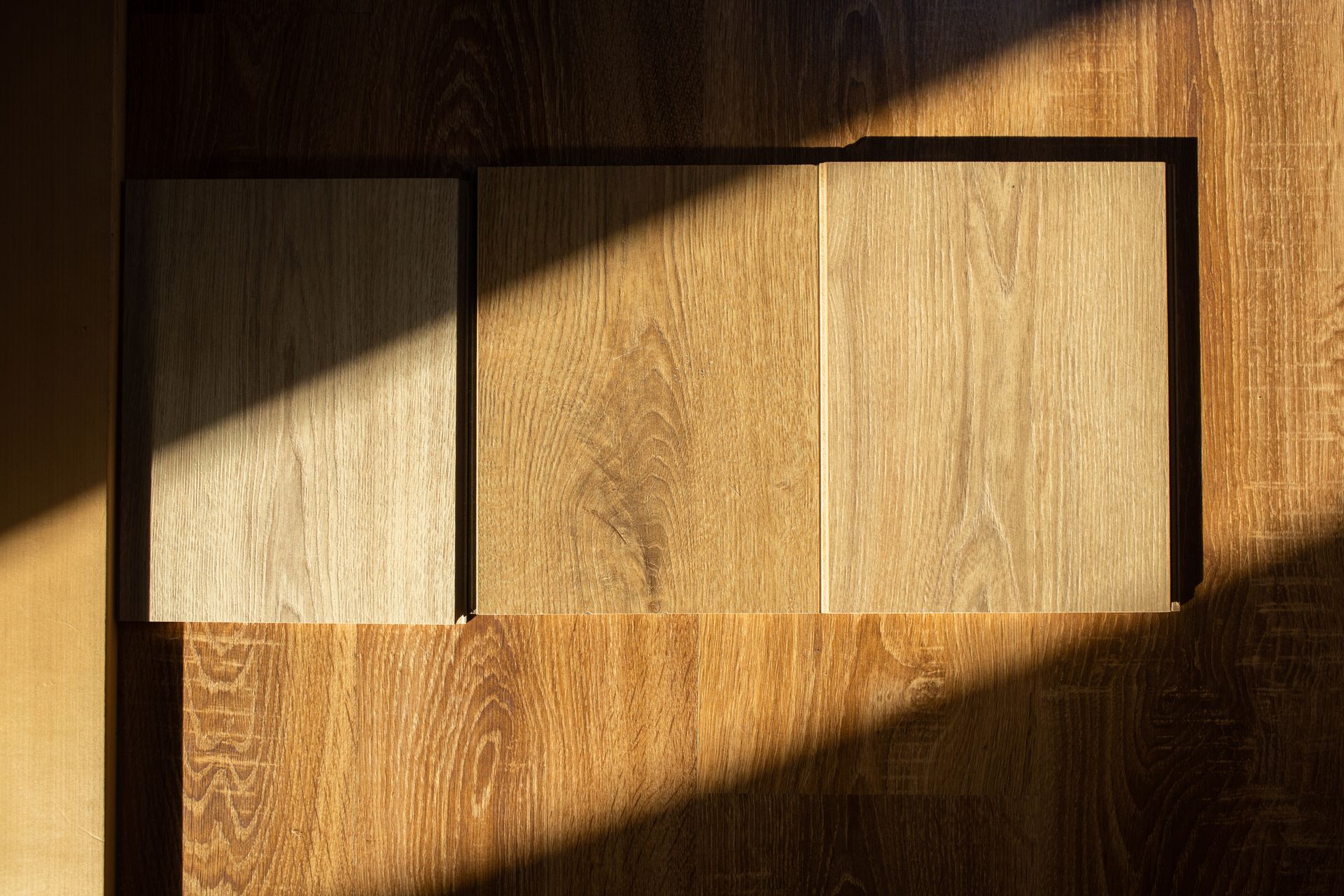 Wooden flooring samples on a wood surface, with sunlight casting shadows.