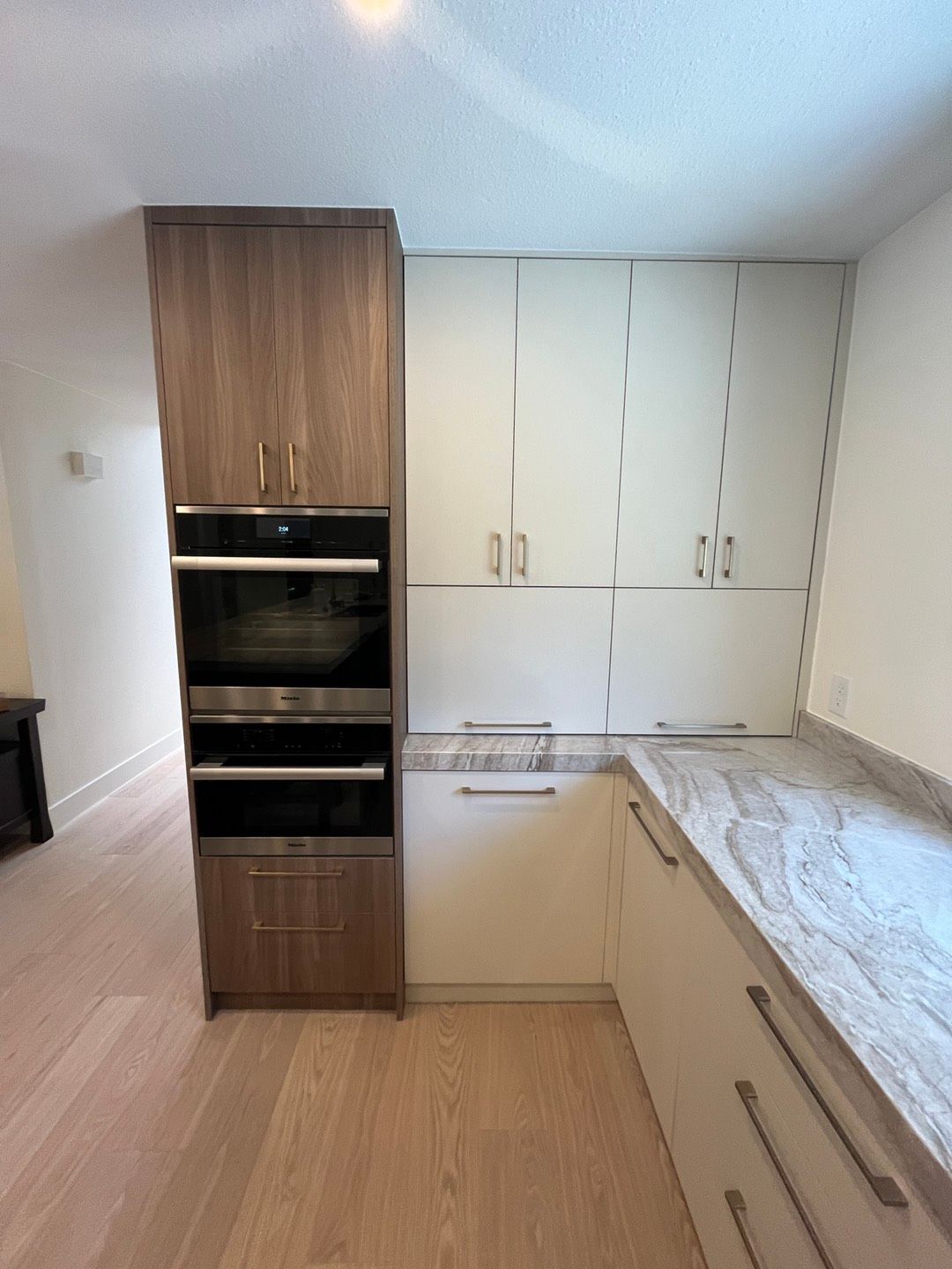 Kitchen cabinetry with built-in oven and microwave. Light wood and white cabinets with granite countertop.