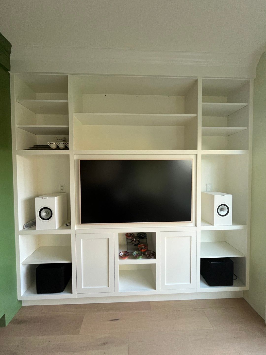 White built-in entertainment center with a TV, shelves, speakers, and cabinets.