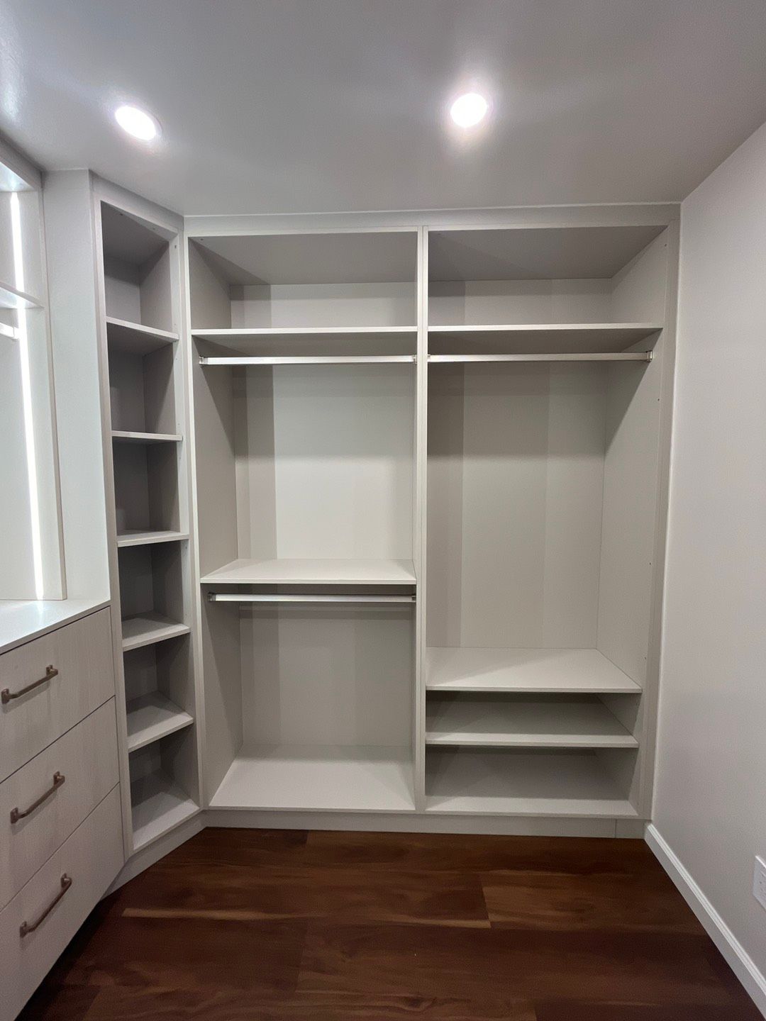 Empty built-in closet with shelves, hanging rods, and drawers; white walls and wood floor.