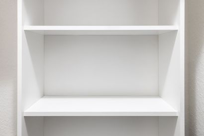 Empty white bookshelf with three shelves against a white wall.