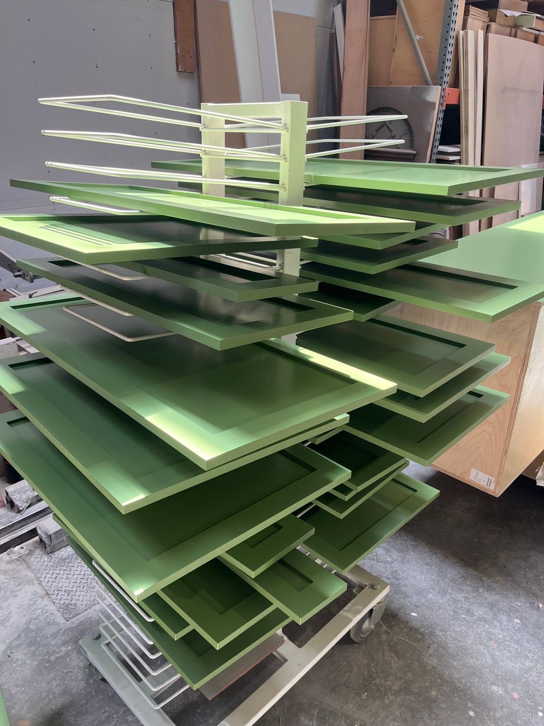 Green cabinet doors stacked on a drying rack in a workshop.