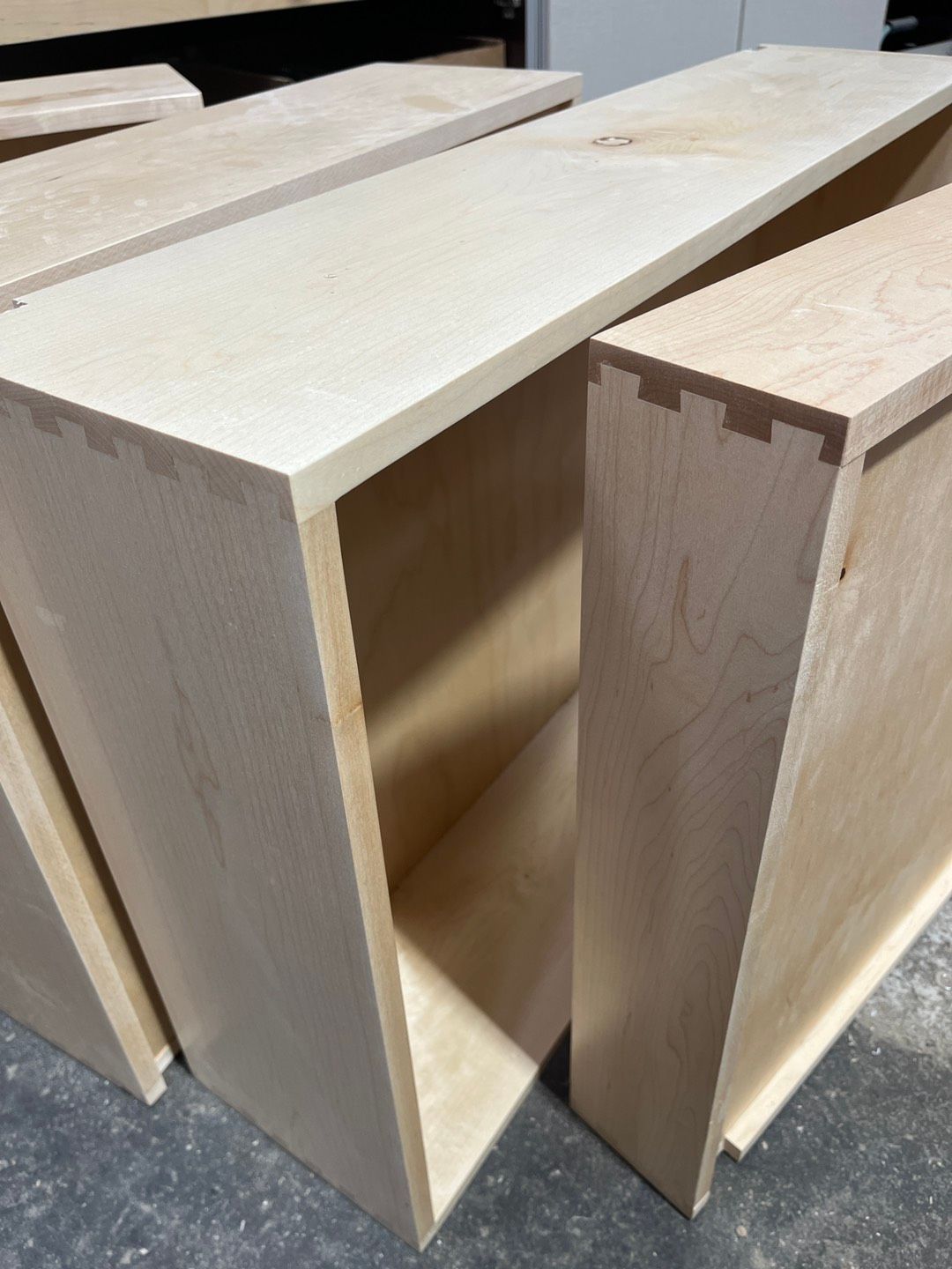 Wooden dovetailed drawer boxes, unfinished, on a concrete surface.