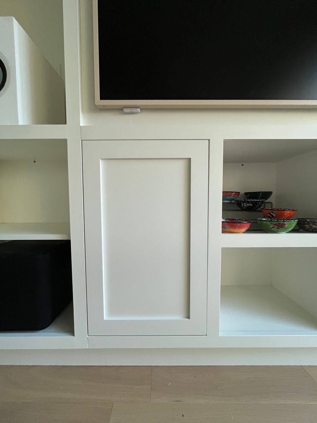 White cabinet door in a built-in entertainment center, with TV above and open shelves to the sides.