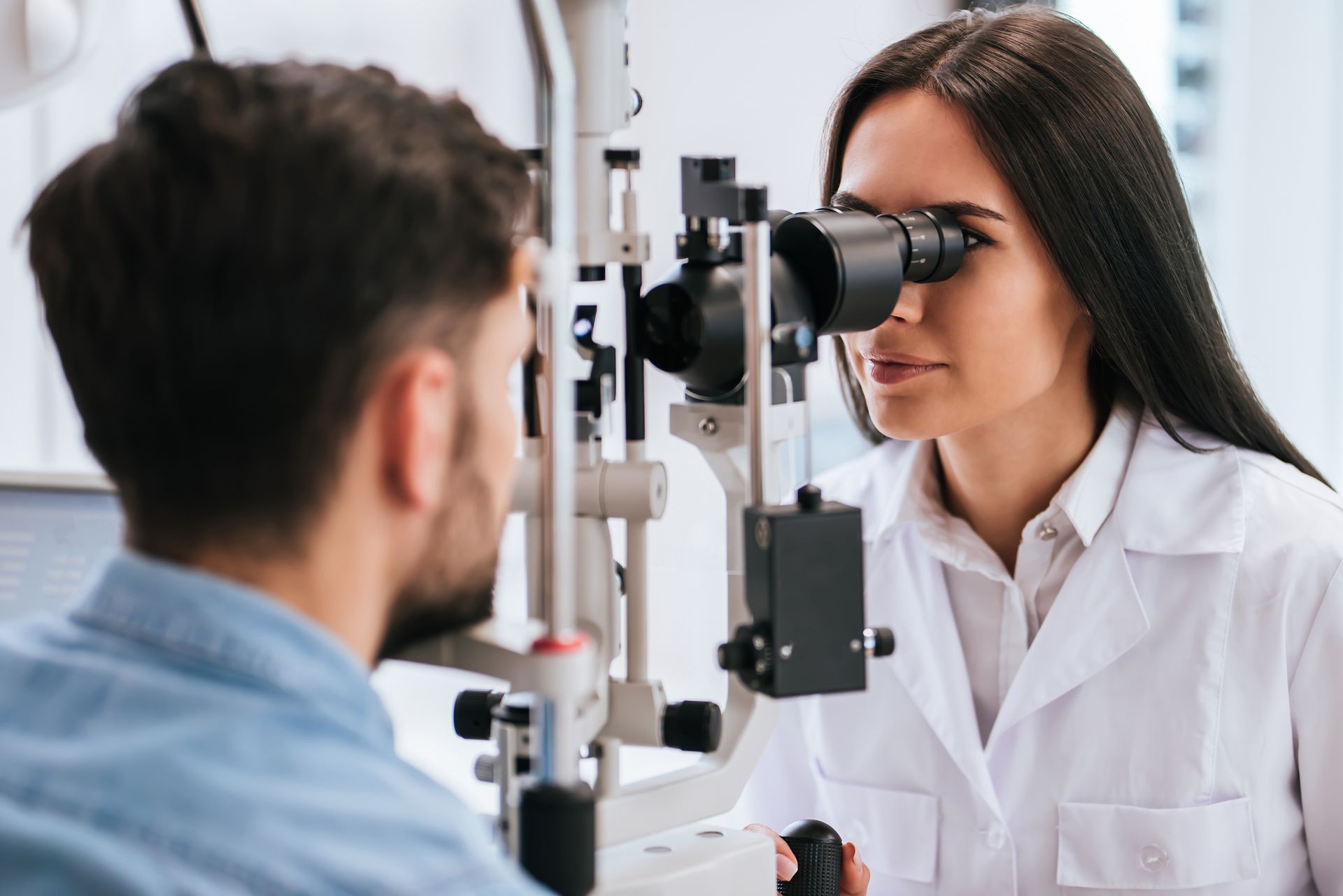 A female eye doctor is doing an eye exam on a man, focusing on the eye chart in front of them.