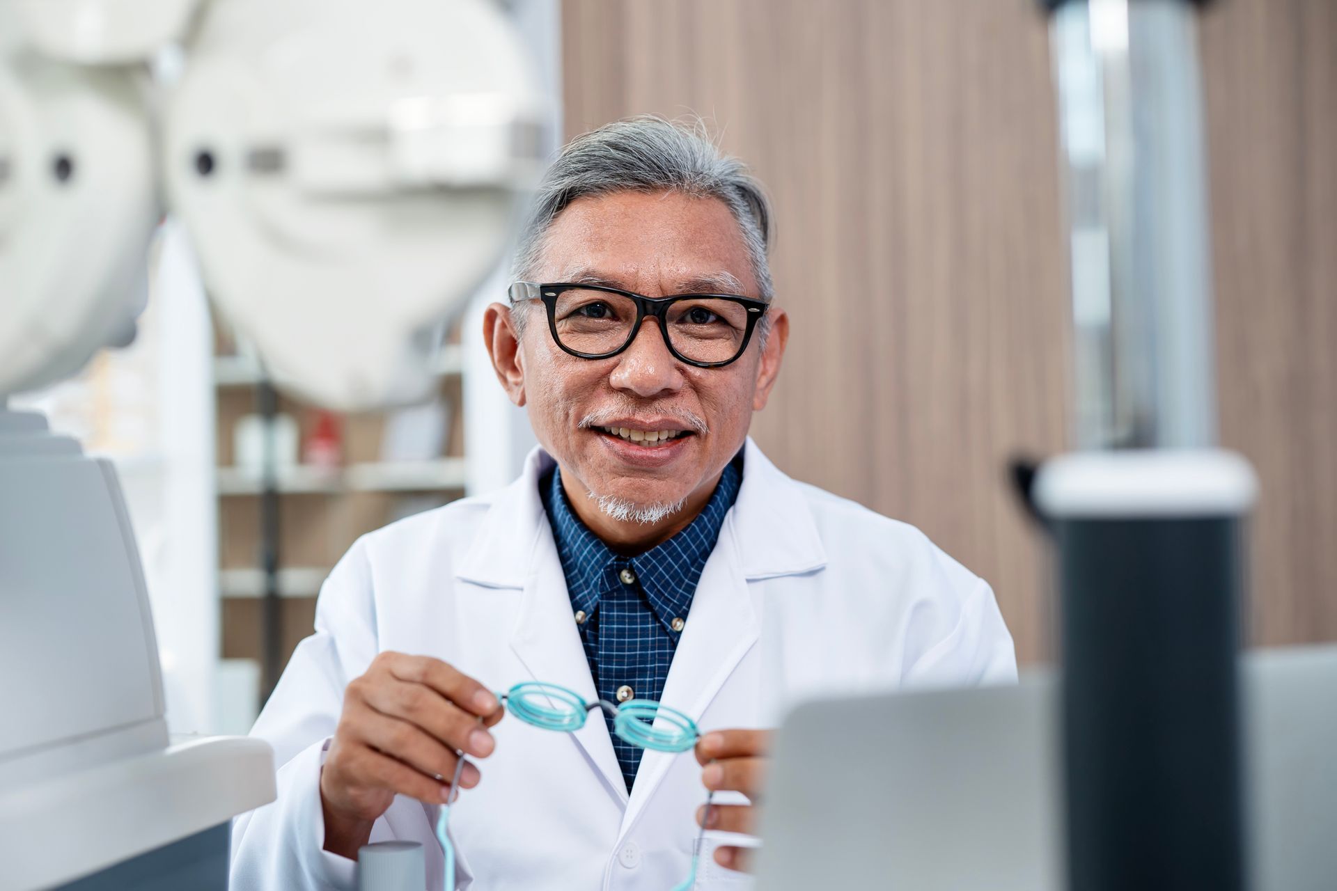 Portrait of a senior male ophthalmologist holding a diopter trial frame during an eye exam.