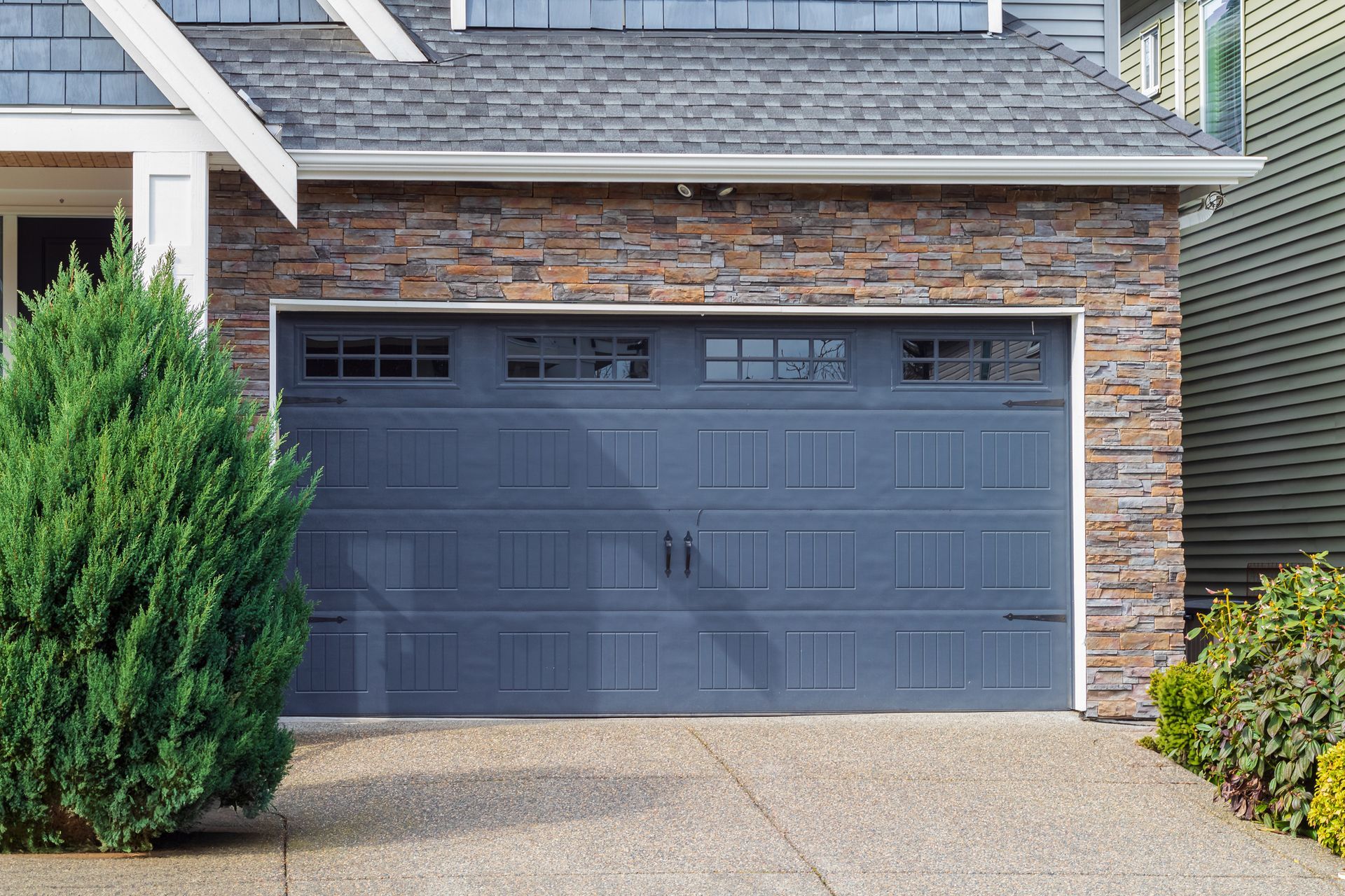 A large gray garage door is sitting in front of a brick house.