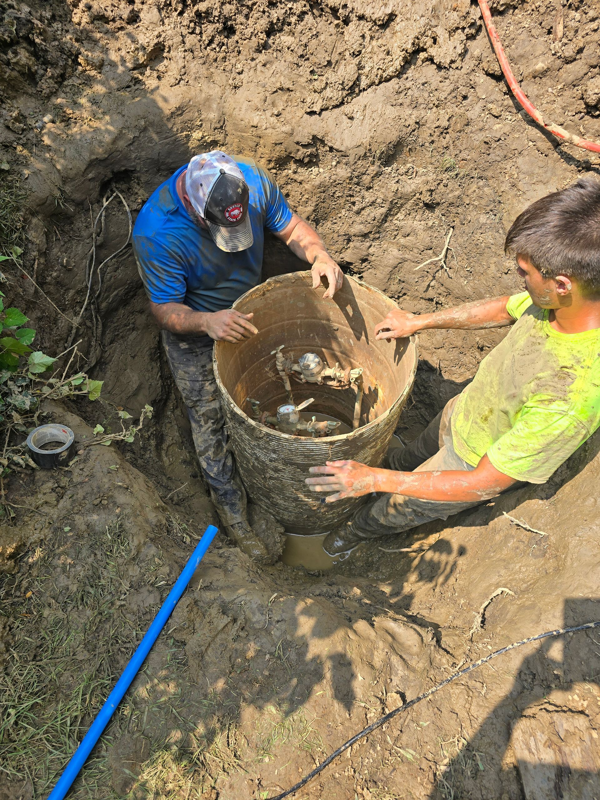 Two men are working on a pipe in the mud.