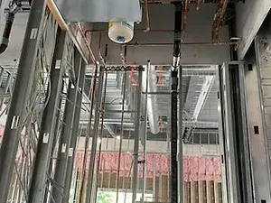 A building under construction with pipes and wires hanging from the ceiling.