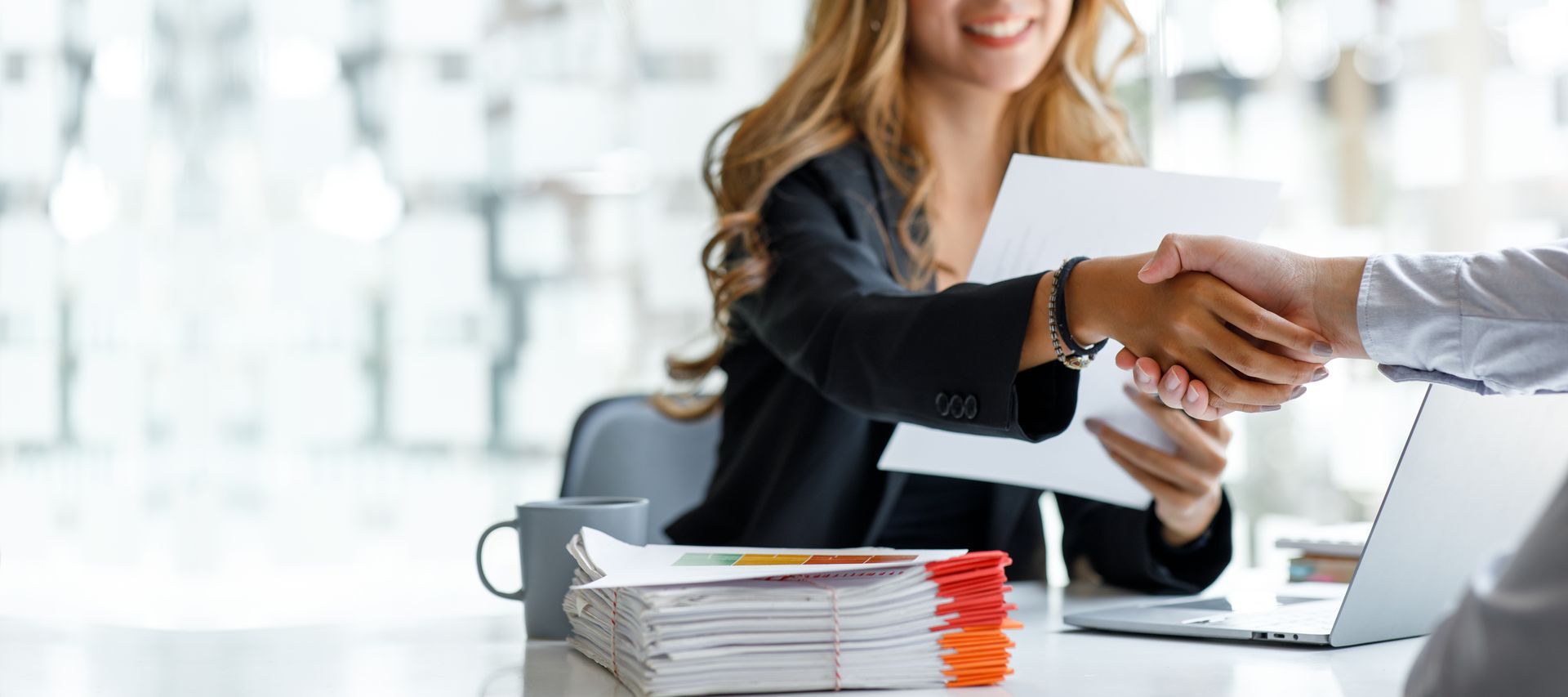 Two people shaking hands during a job interview at an office desk with documents and a laptop. Two people shaking hands during a job interview at an office desk with documents and a laptop.