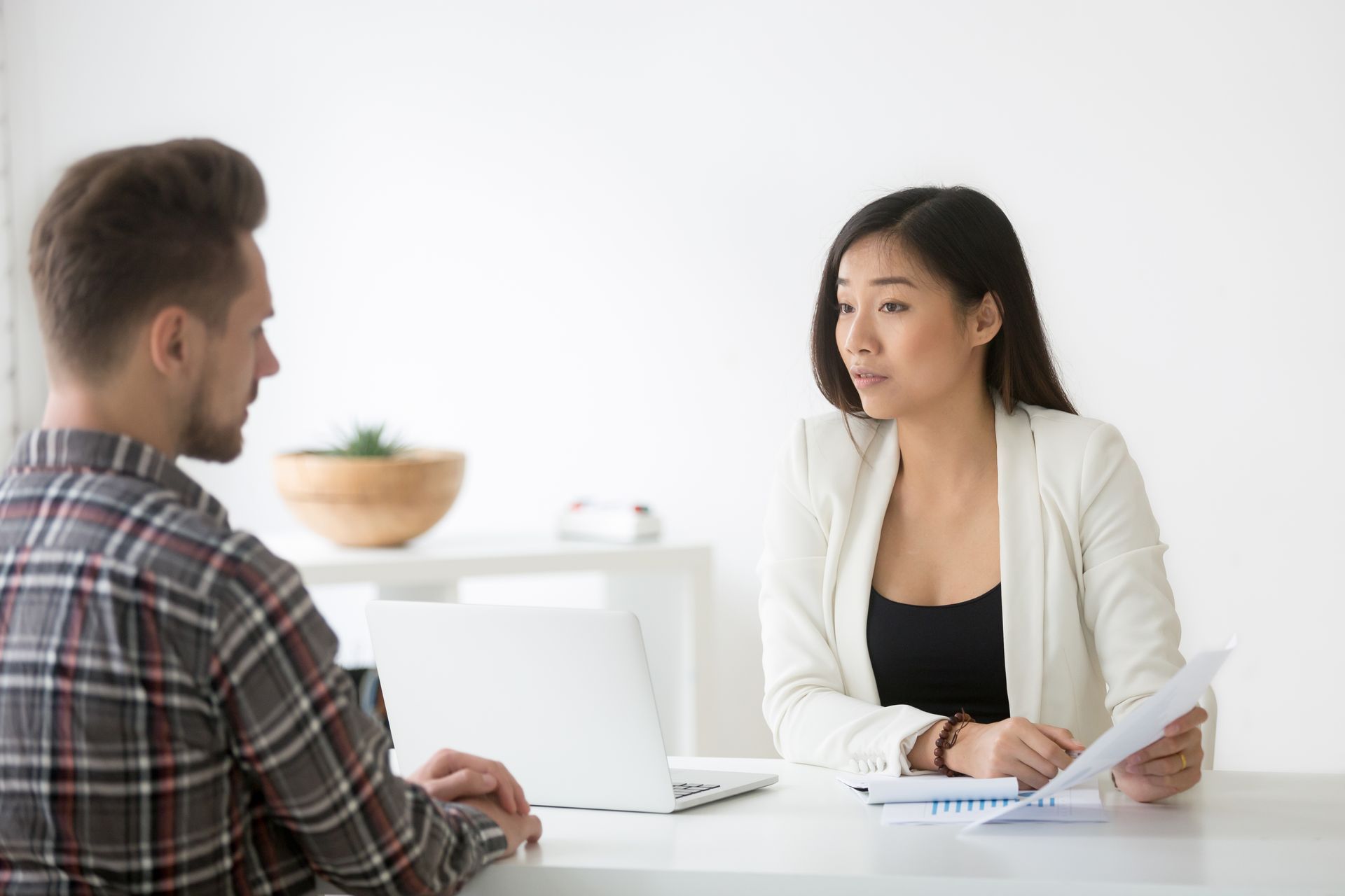 Businesswoman siting in a white table discusses a document with a man sitting in front of him.