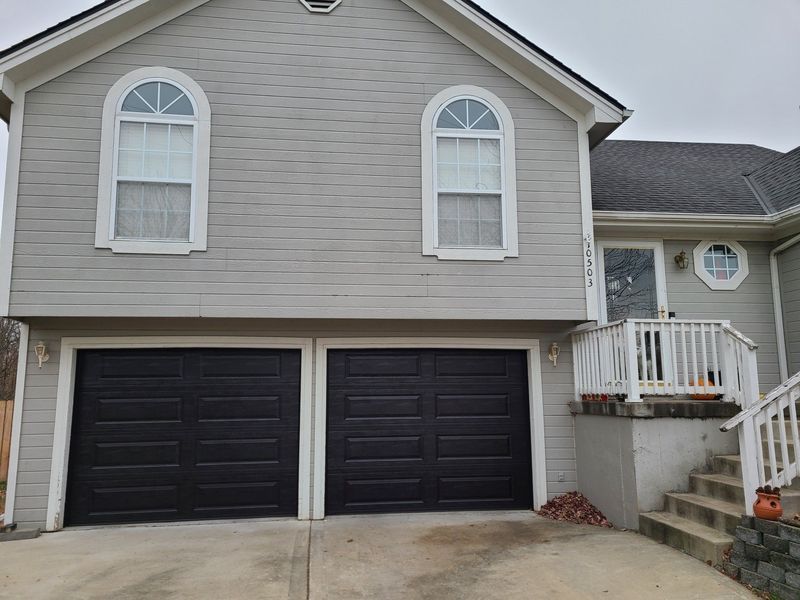Two-story house with gray siding, black garage doors, and arched windows. Concrete driveway.