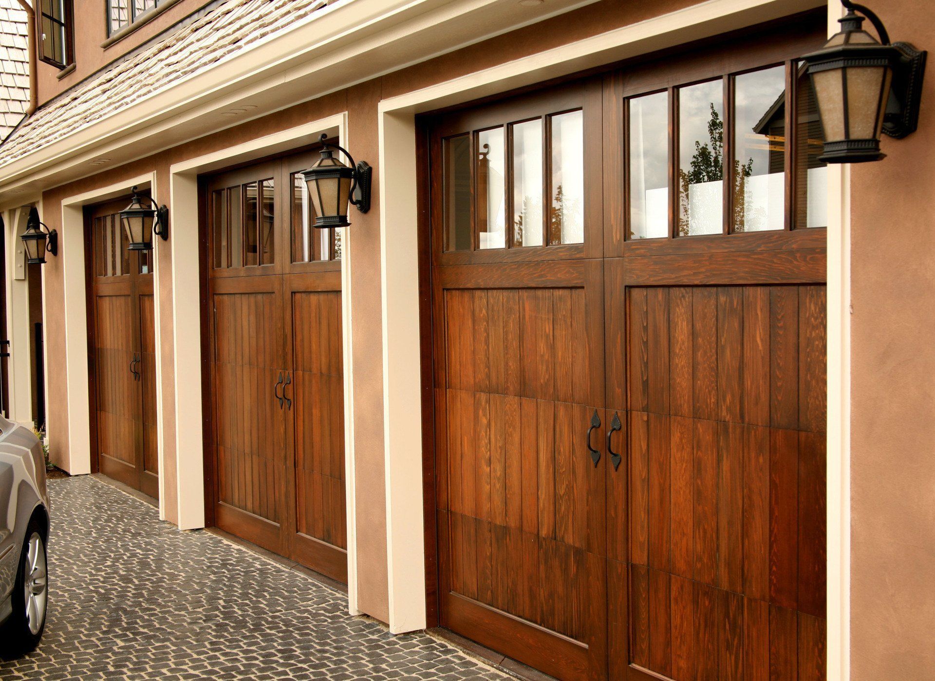 Three brown wooden garage doors with glass windows and black lanterns.