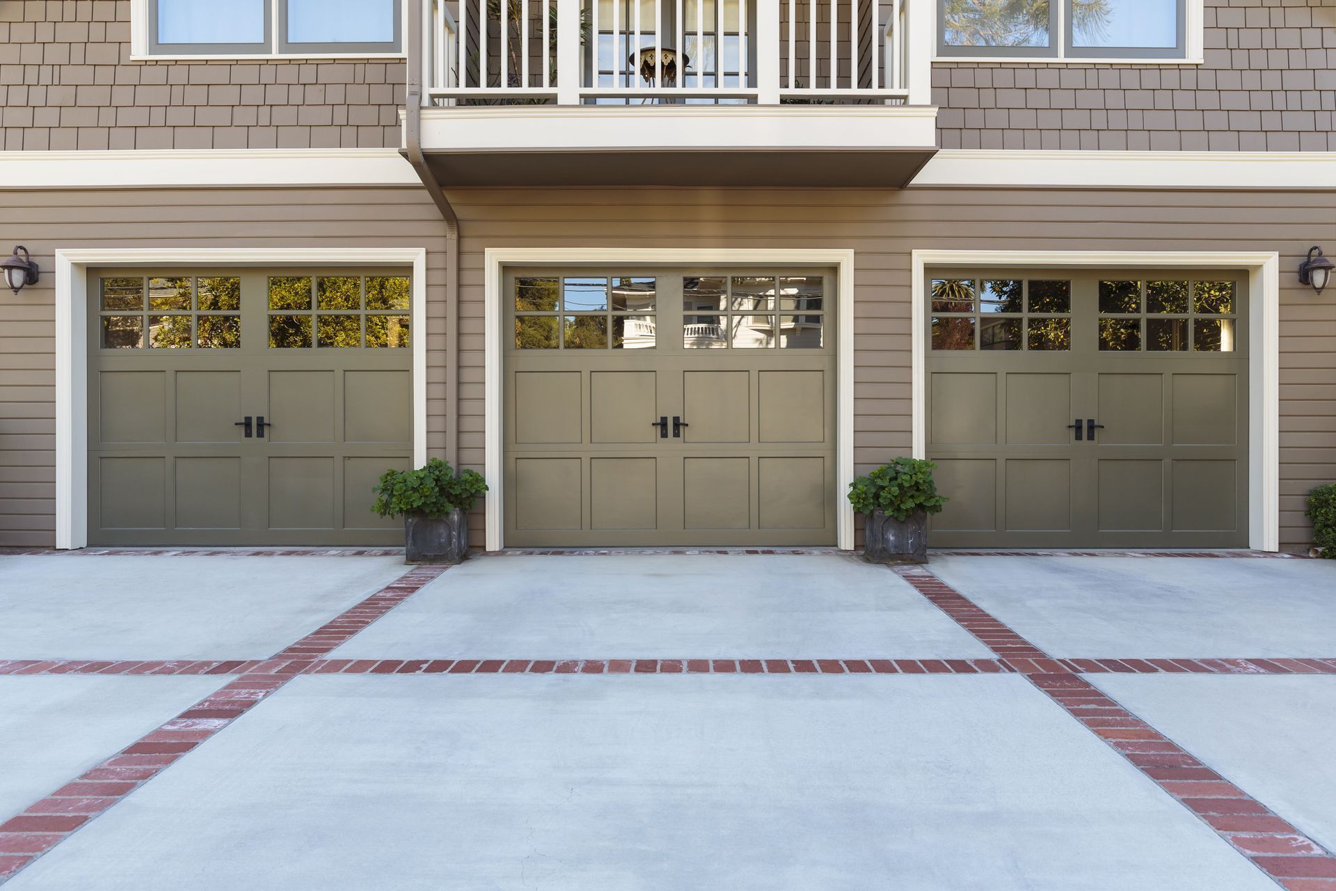 Three olive-green garage doors with windows in a tan building; potted plants sit in front.
