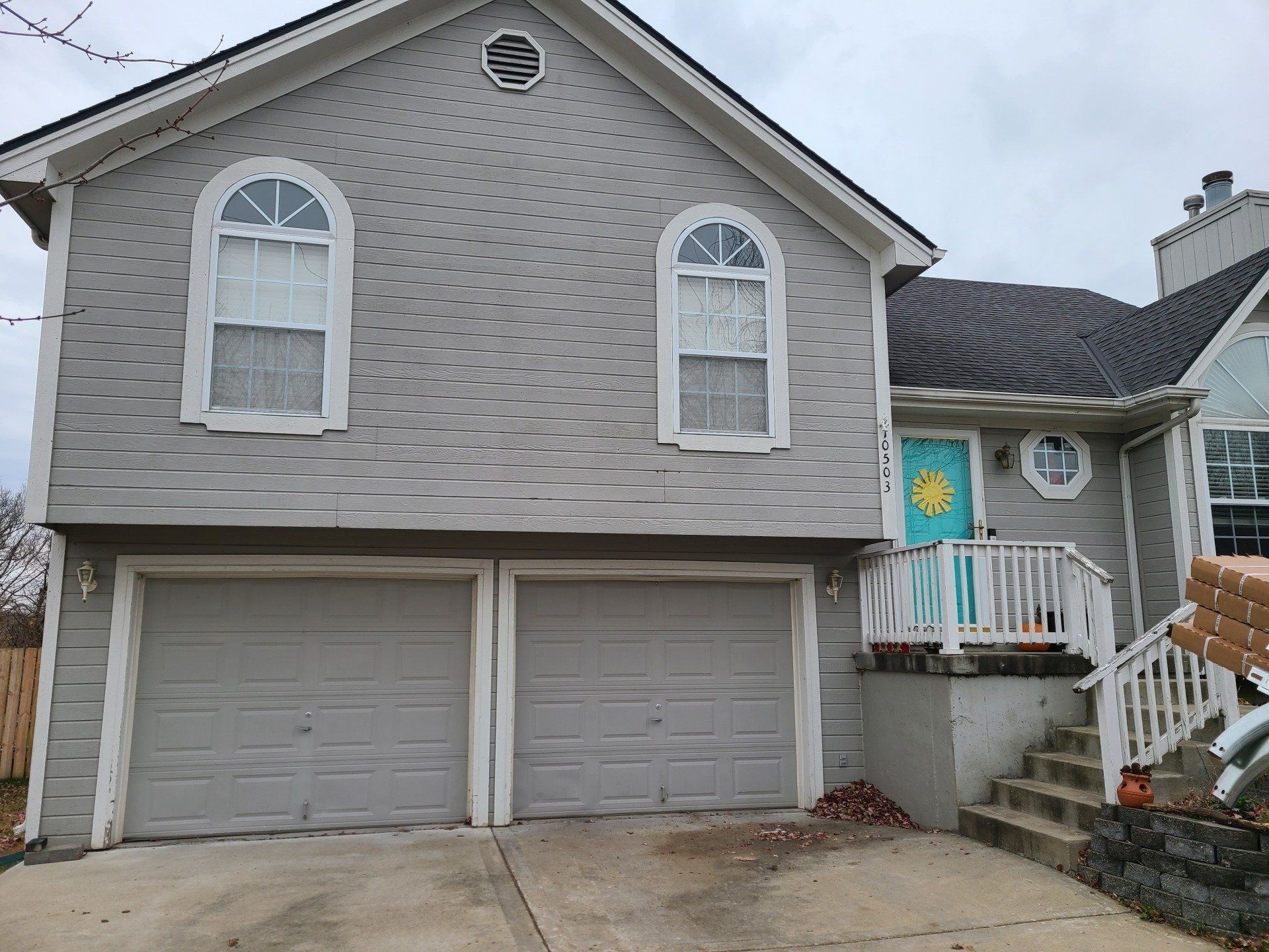 Gray two-story house with arched windows and two-car garage. Turquoise door and white trim. Gray roof.