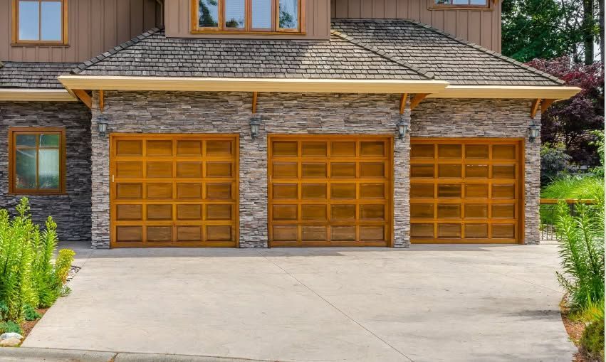 A three-car garage with brown doors, set in a stone facade, and a concrete driveway.
