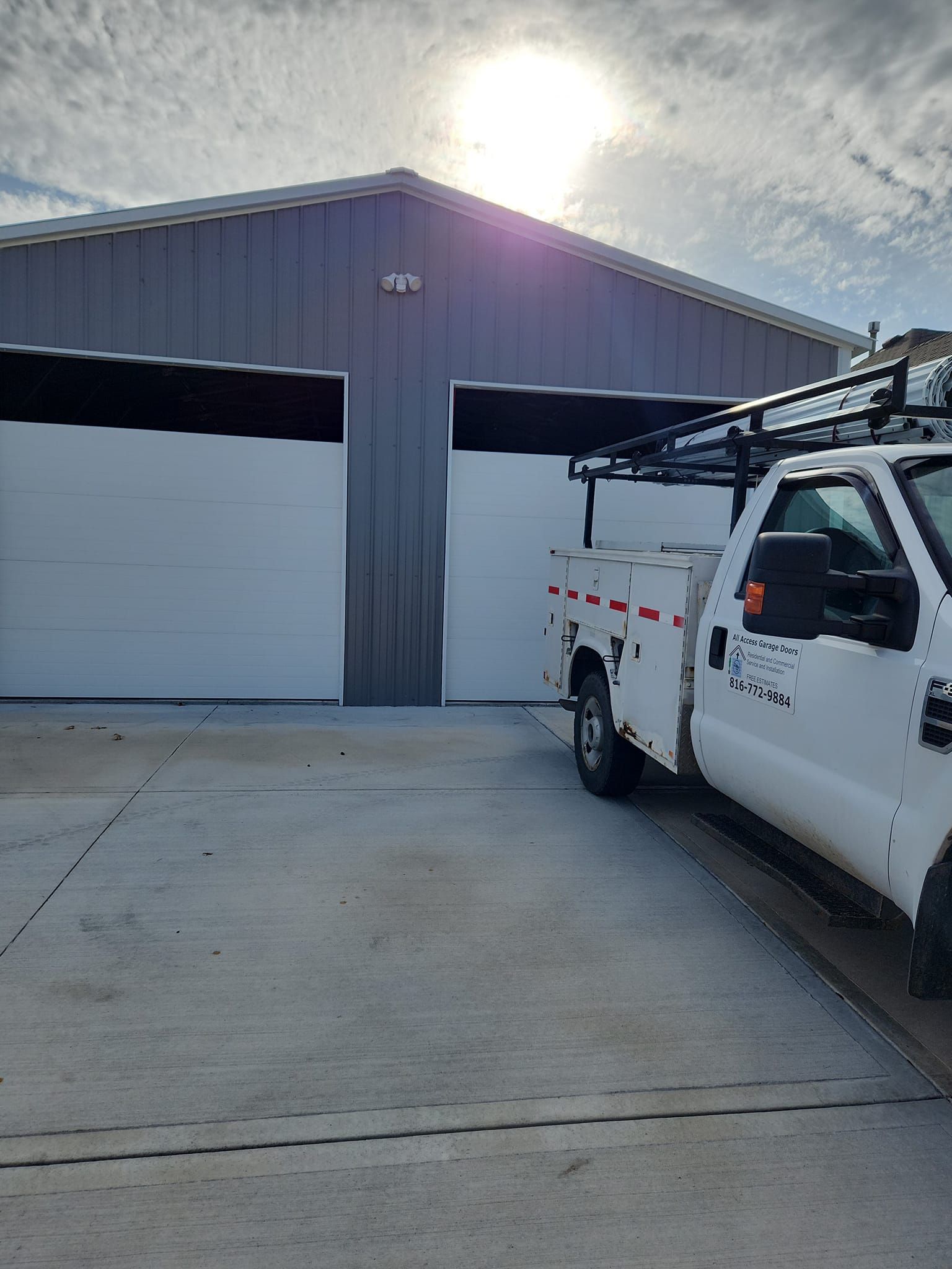 White work truck parked in front of a gray metal building with two white garage doors, sunny sky.