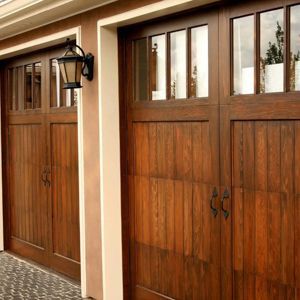 Two brown wooden garage doors with windows, a dark wall lamp, and a beige door frame.