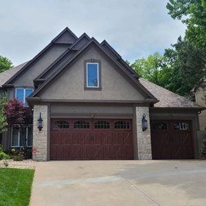 Two-story house with brown garage doors, tan siding, and stone accents.