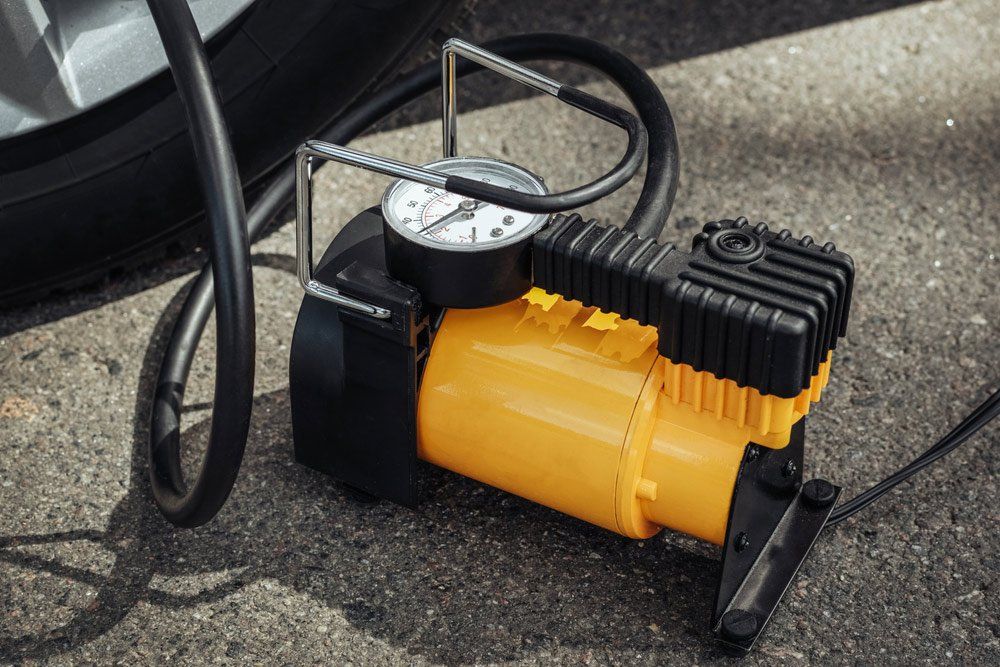 A Yellow Air Compressor is Sitting Next to a Tire on the Ground — SVS Auto Repairs & Dyno Tuning in Weipa, QLD