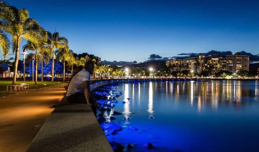 A Man is Sitting on a Pier Overlooking a Body of Water at Night — SVS Auto Repairs & Dyno Tuning in Cairns, QLD