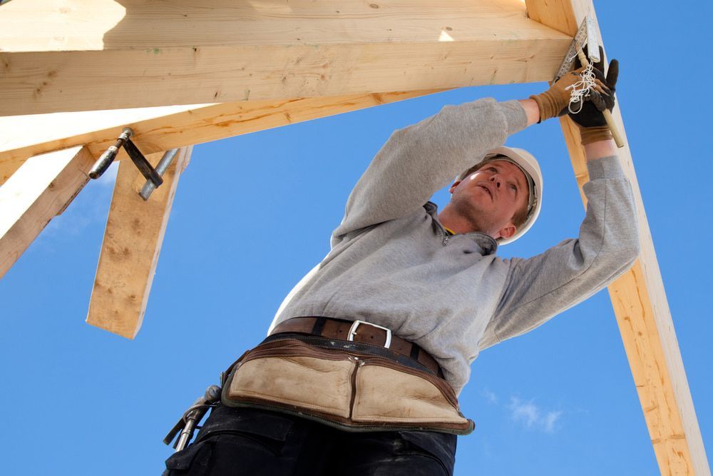 A Man Wearing A Hard Hat Is Working On A Wooden Structure — Hitek Frame & Truss In Dubbo, NSW
