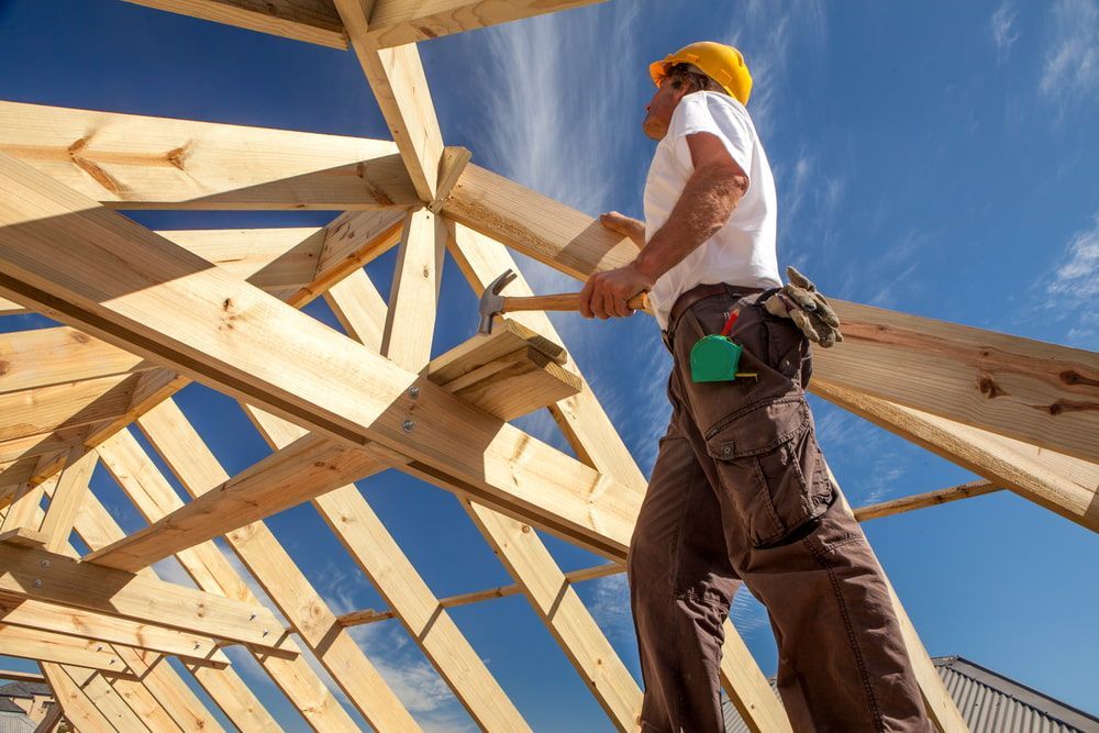 A Man Is Standing On Top Of A Wooden Structure Holding A Hammer — Hitek Frame & Truss In Warren, NSW