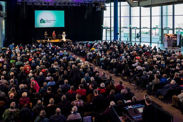 Die Außenwärmepumpe ist an einer Backsteinmauer neben einer Topfpflanze montiert.