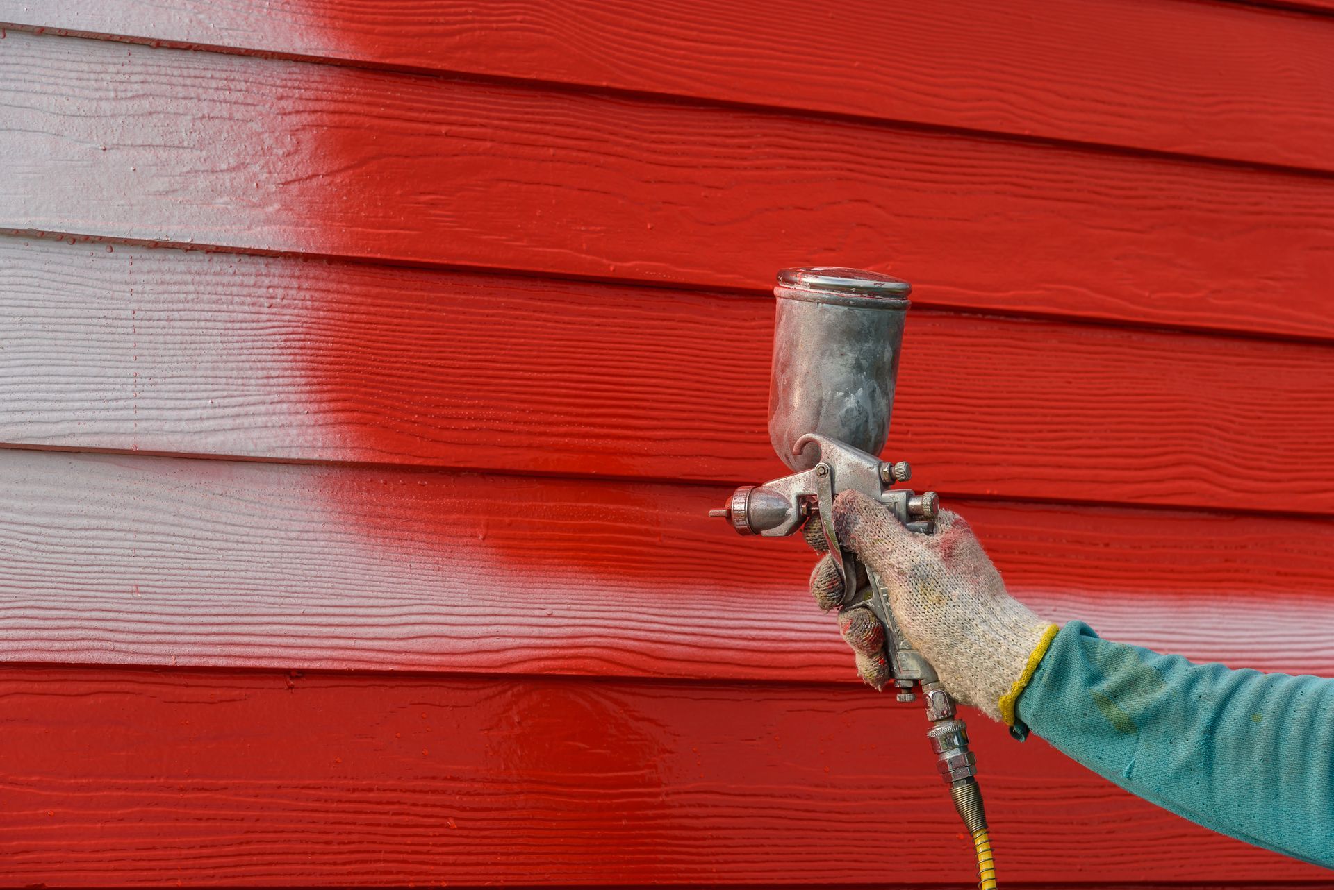 A person is spray painting a red siding on a house.