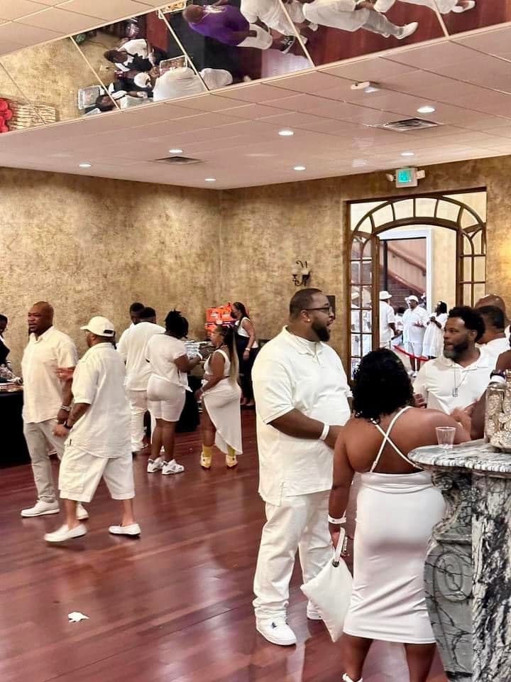 People in white attire socialize in a room with a mirrored ceiling.