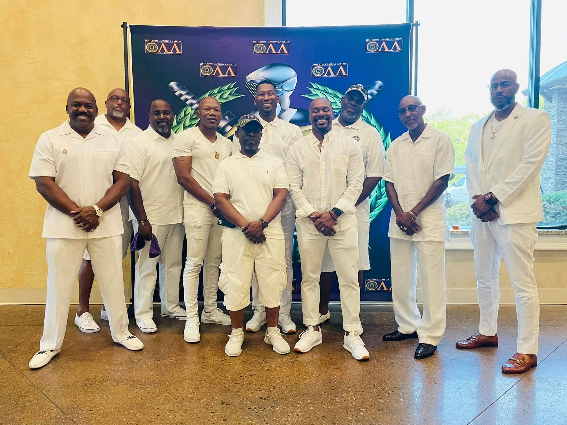 Group of men in white outfits posing in front of a banner.