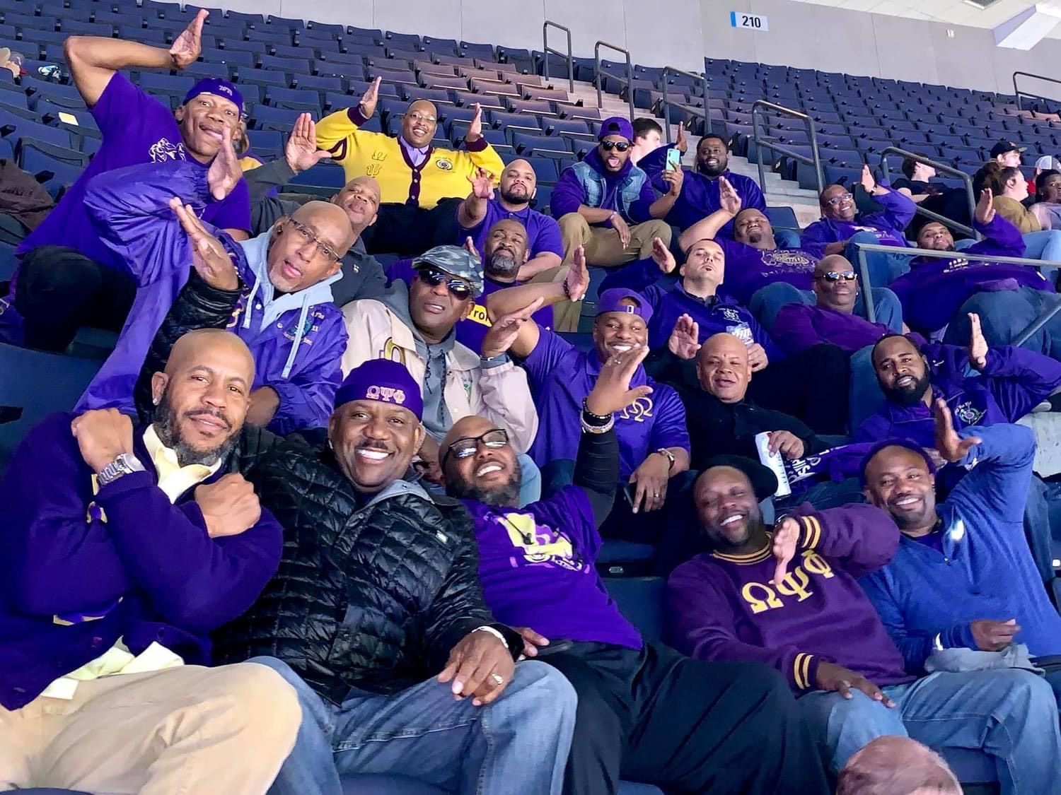 Group of men in purple at an event, some smiling and raising hands.