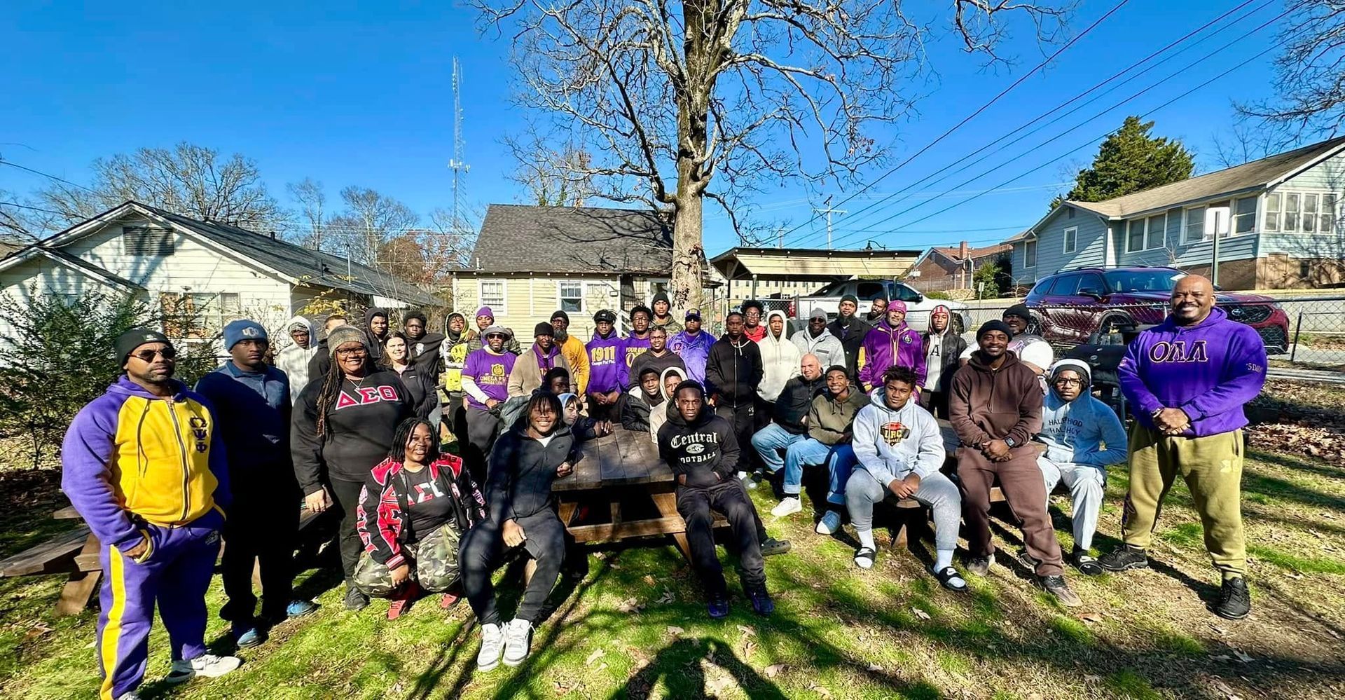 Group of people in purple and gold attire pose outside on a sunny day.