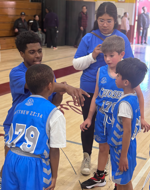 A person wearing a hat and orange shirt, holding a baseball bat on their shoulder on a baseball field.