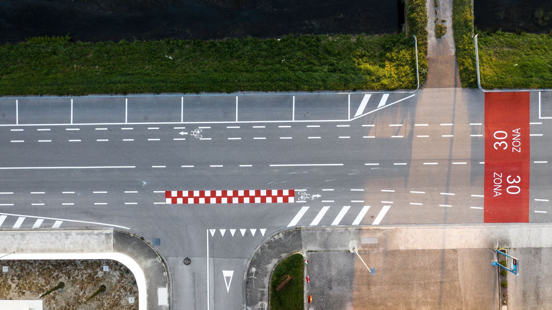 Vista dall'alto di un incrocio stradale con segnaletica orizzontale bianca, pista ciclabile rossa.
