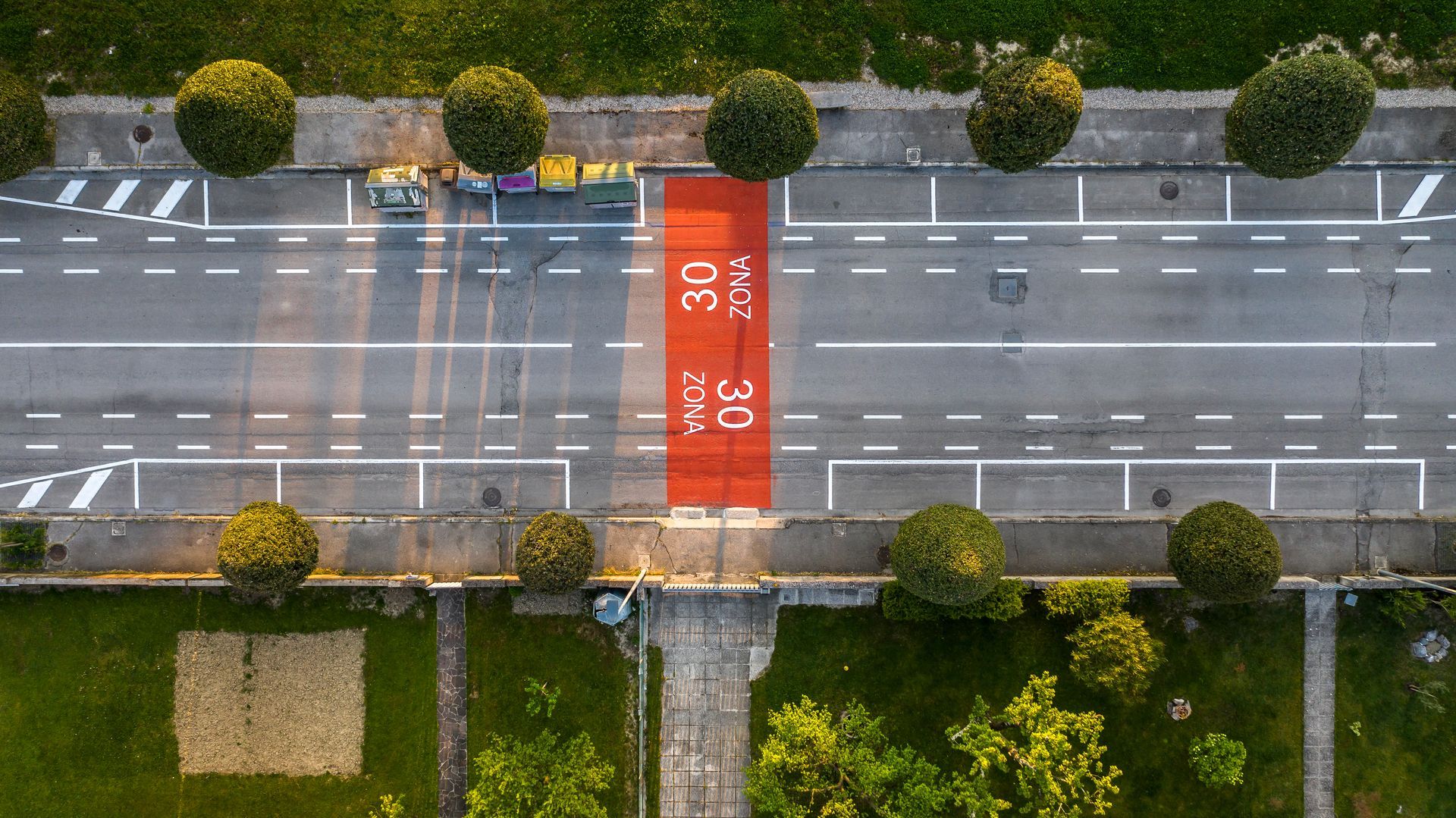 Vista dall'alto di una strada con una zona con limite di velocità di 30 km/h contrassegnata in rosso, fiancheggiata da alberi e attraversamento pedonale.