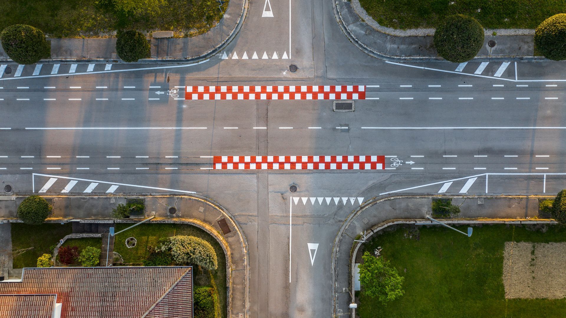 Vista dall'alto di un incrocio con attraversamenti pedonali, due dossi rallentatori a strisce rosse e bianche e aree verdi.