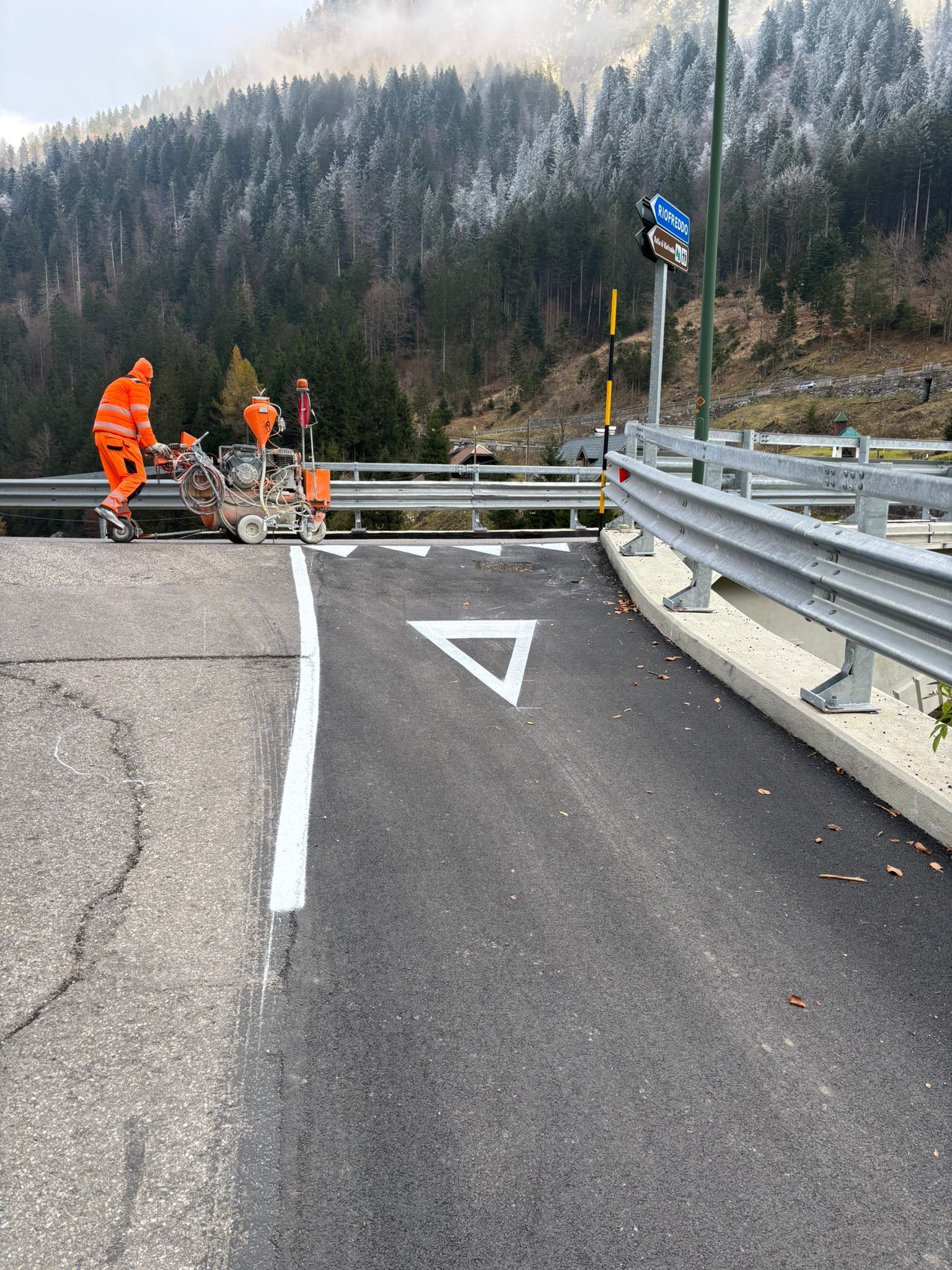 Operai stradali che dipingono un cartello di precedenza e una linea di demarcazione su una strada di montagna.