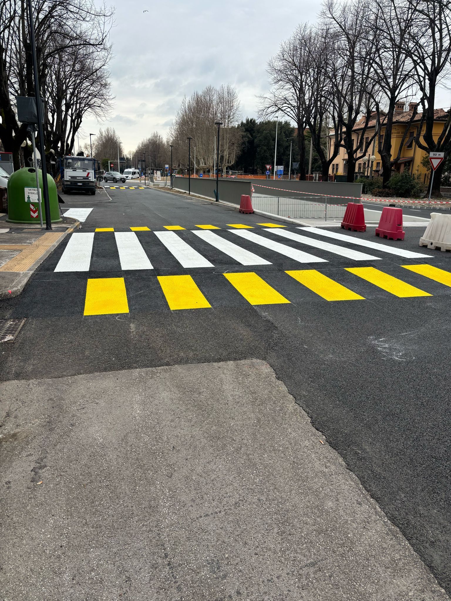 Attraversamento pedonale con strisce gialle e bianche su strada asfaltata. 