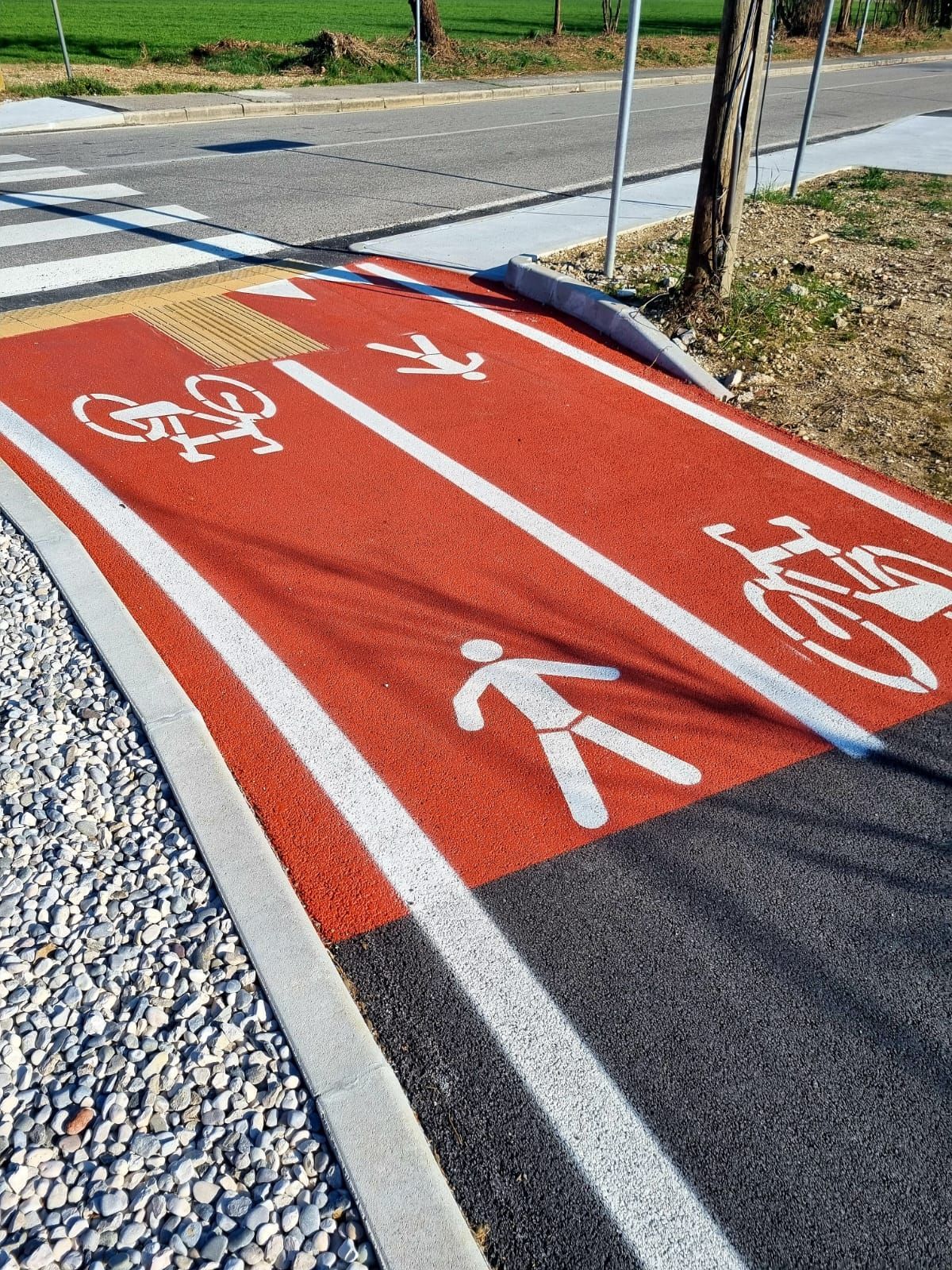 Pista ciclabile e pedonale rossa con segnaletica e simboli bianchi.
