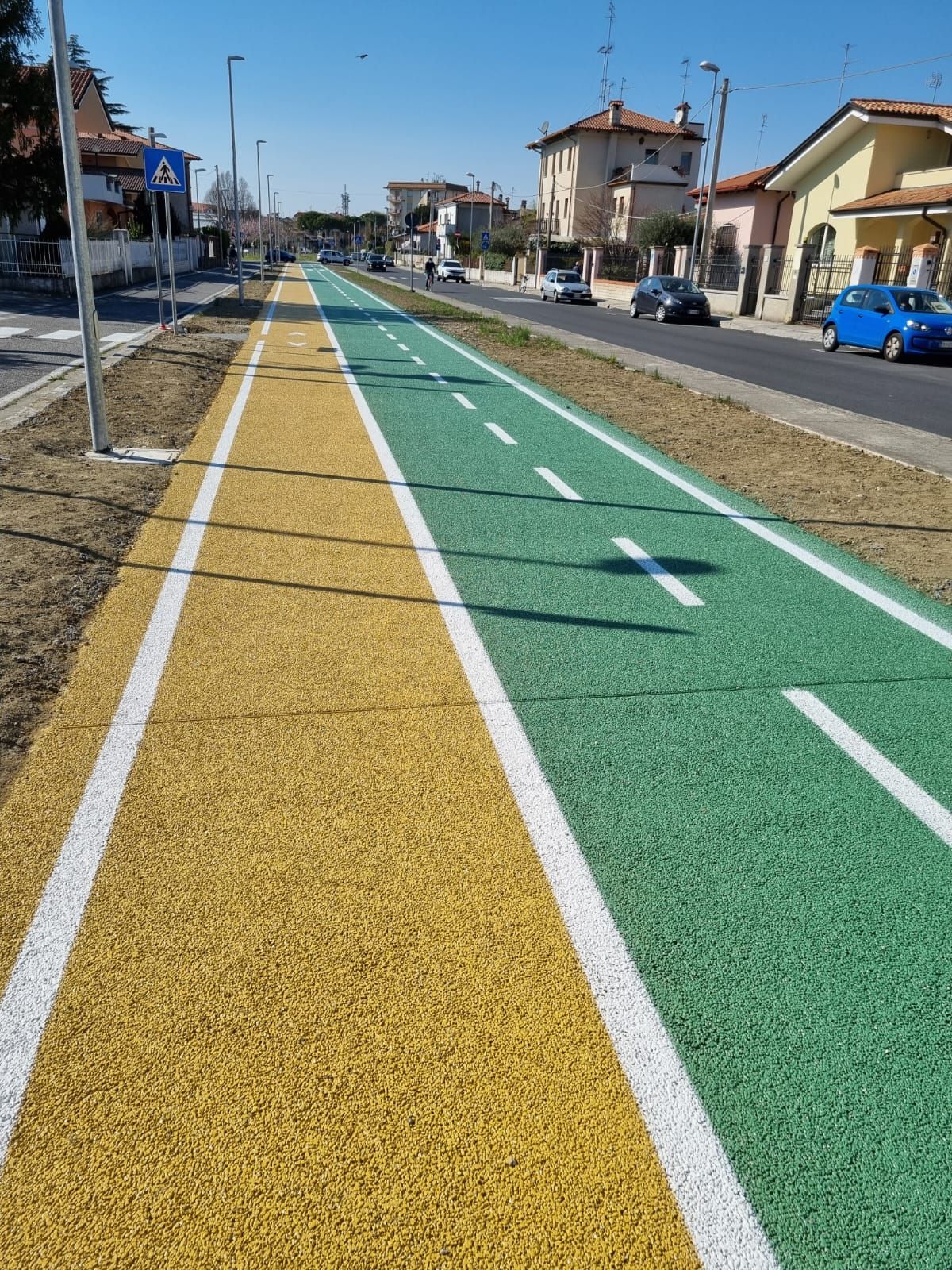 Una pista ciclabile multicolore, verde e gialla, lungo una strada con automobili ed edifici.