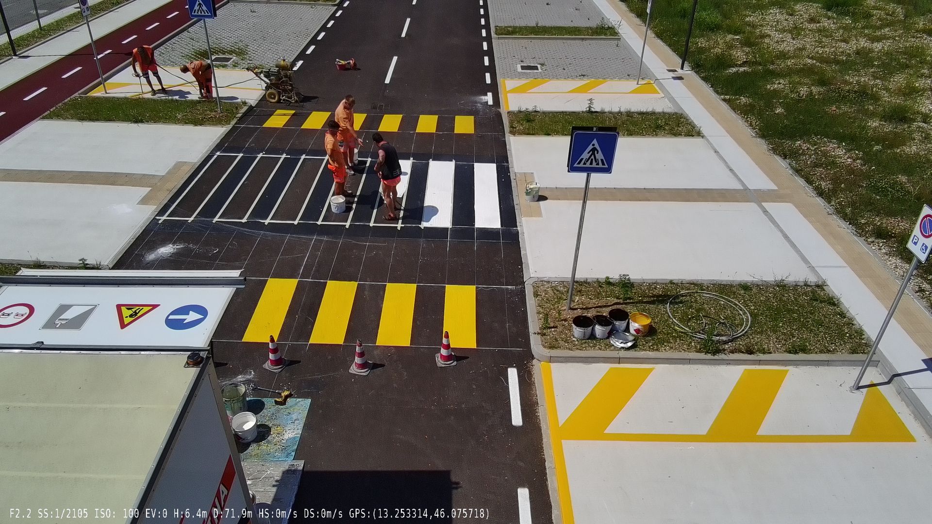Vista aerea di una strada, attraversamenti pedonali, segnaletica di stop, semafori e parcheggi.
