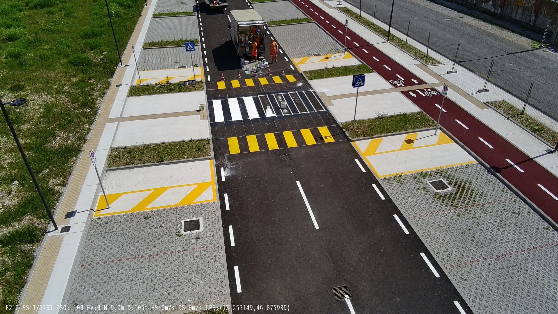 Vista aerea di una strada, attraversamenti pedonali, segnaletica di stop, semafori e parcheggi.