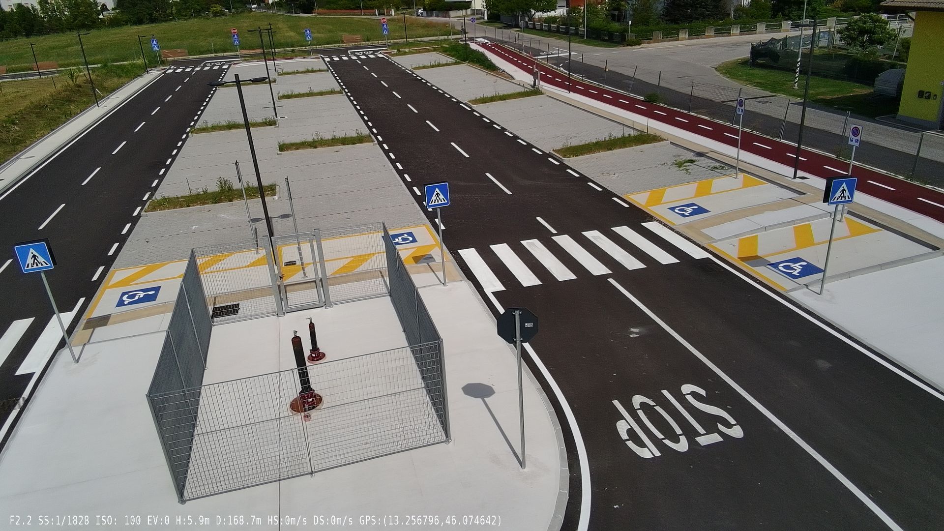 Vista aerea di una strada, attraversamenti pedonali, segnaletica di stop, semafori e parcheggi.