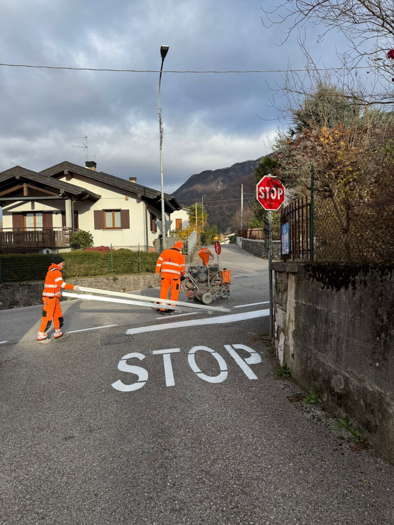 Gli operai stradali con i giubbotti arancioni dipingono le strisce pedonali in corrispondenza di un segnale di stop in una strada residenziale.