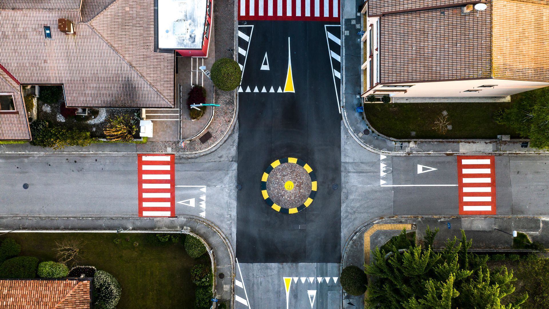 Vista dall'alto di un incrocio stradale con attraversamenti pedonali, segnaletica orizzontale dipinta e una rotonda centrale.