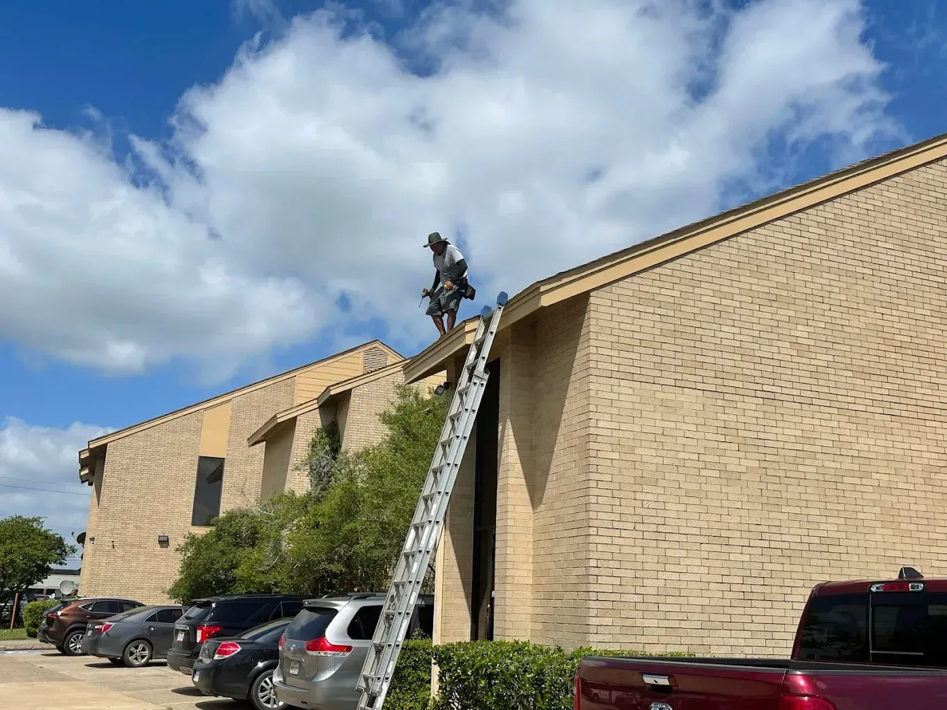 A person on a roof repairs shingles, using a ladder for access
