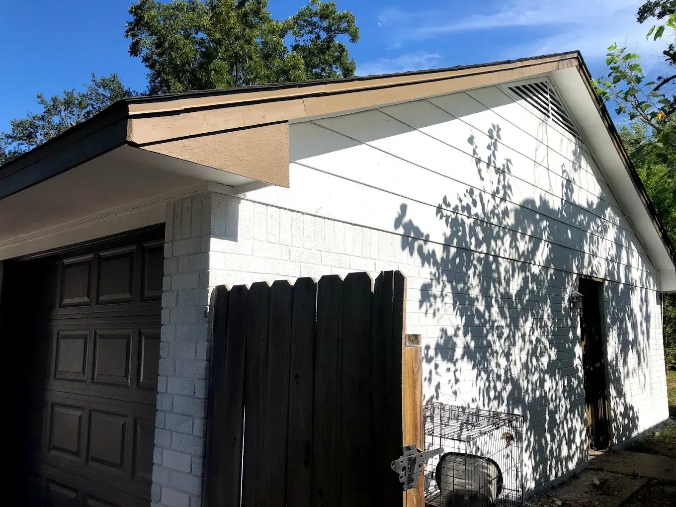 A white garage with a brown roof and garage door. The walls are partially brick and wood.